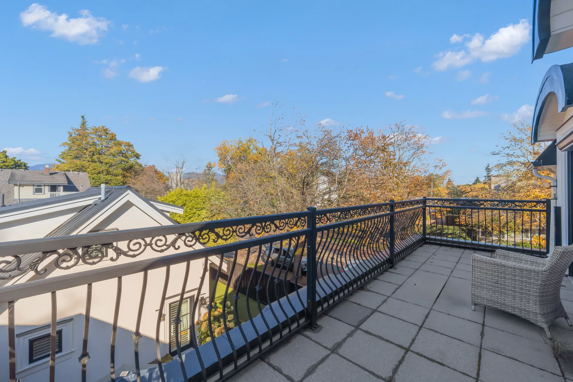 The balcony the other way: the iron railing, a wicker chair, the treetops of West Point Grey