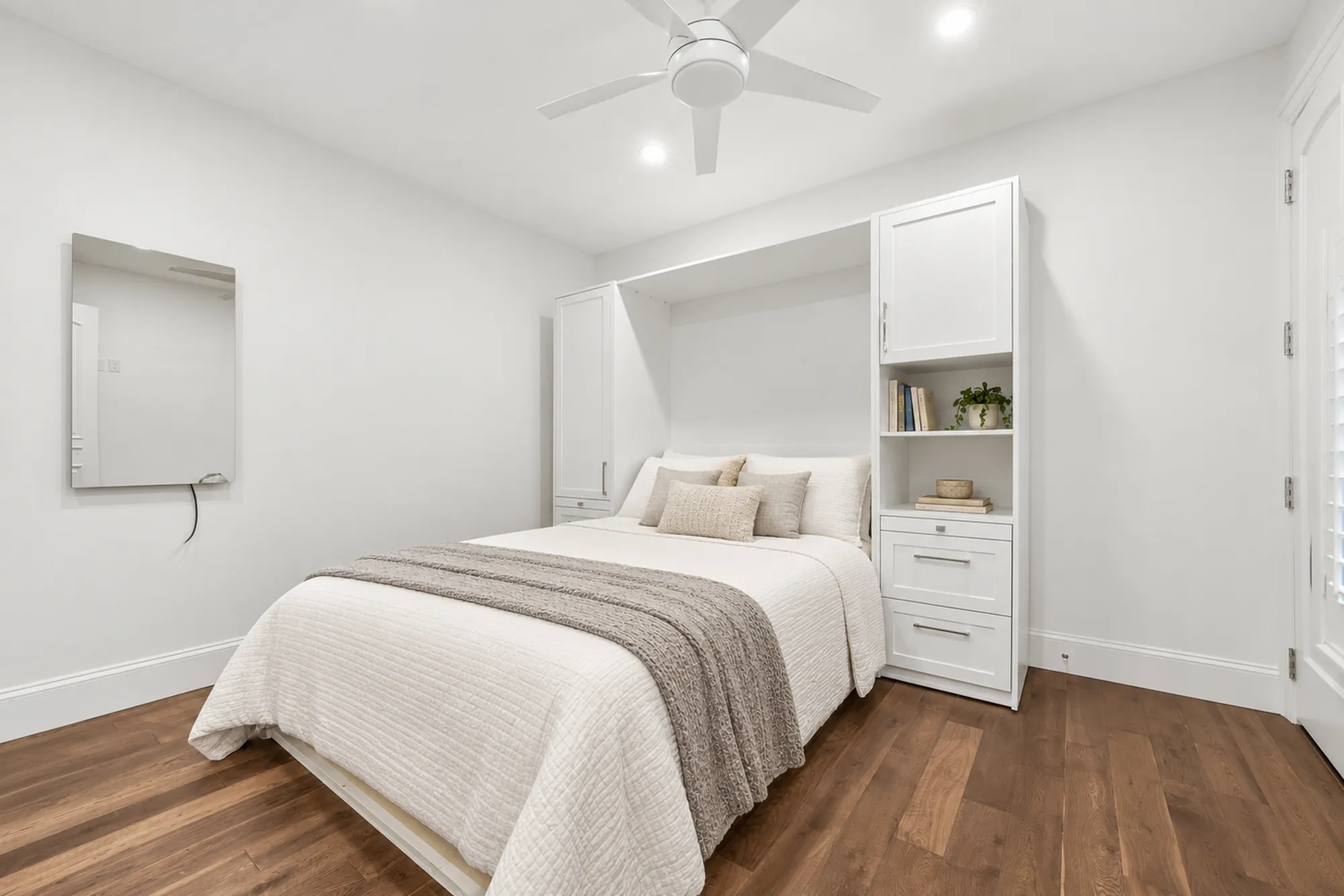 The lower bedroom virtually staged: a bed in a white wall unit with shelves and drawers, linen bedding, a ceiling fan