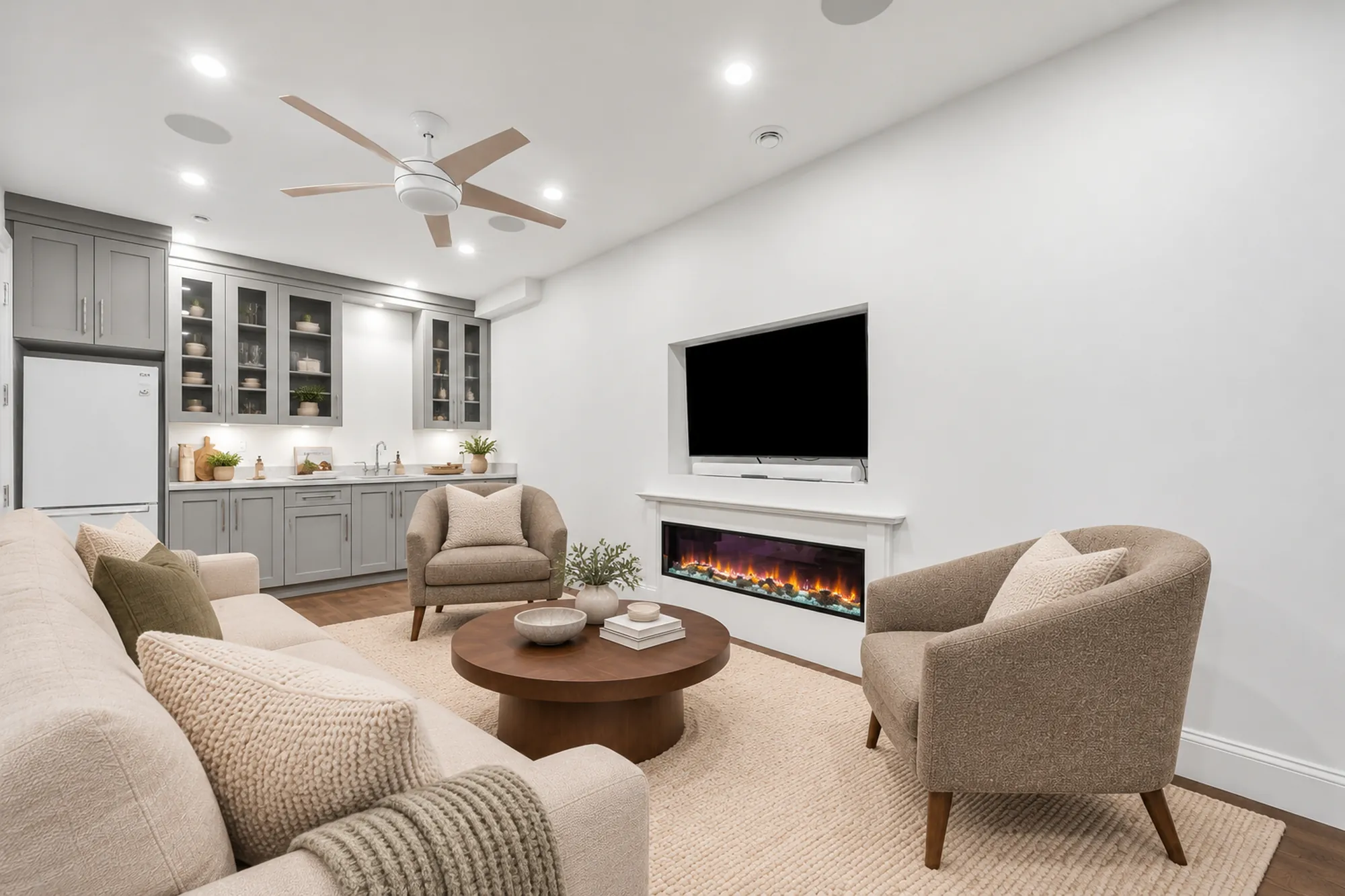 The family room toward the wet bar, virtually staged: grey cabinets with glass doors, a refrigerator, armchairs and a sofa