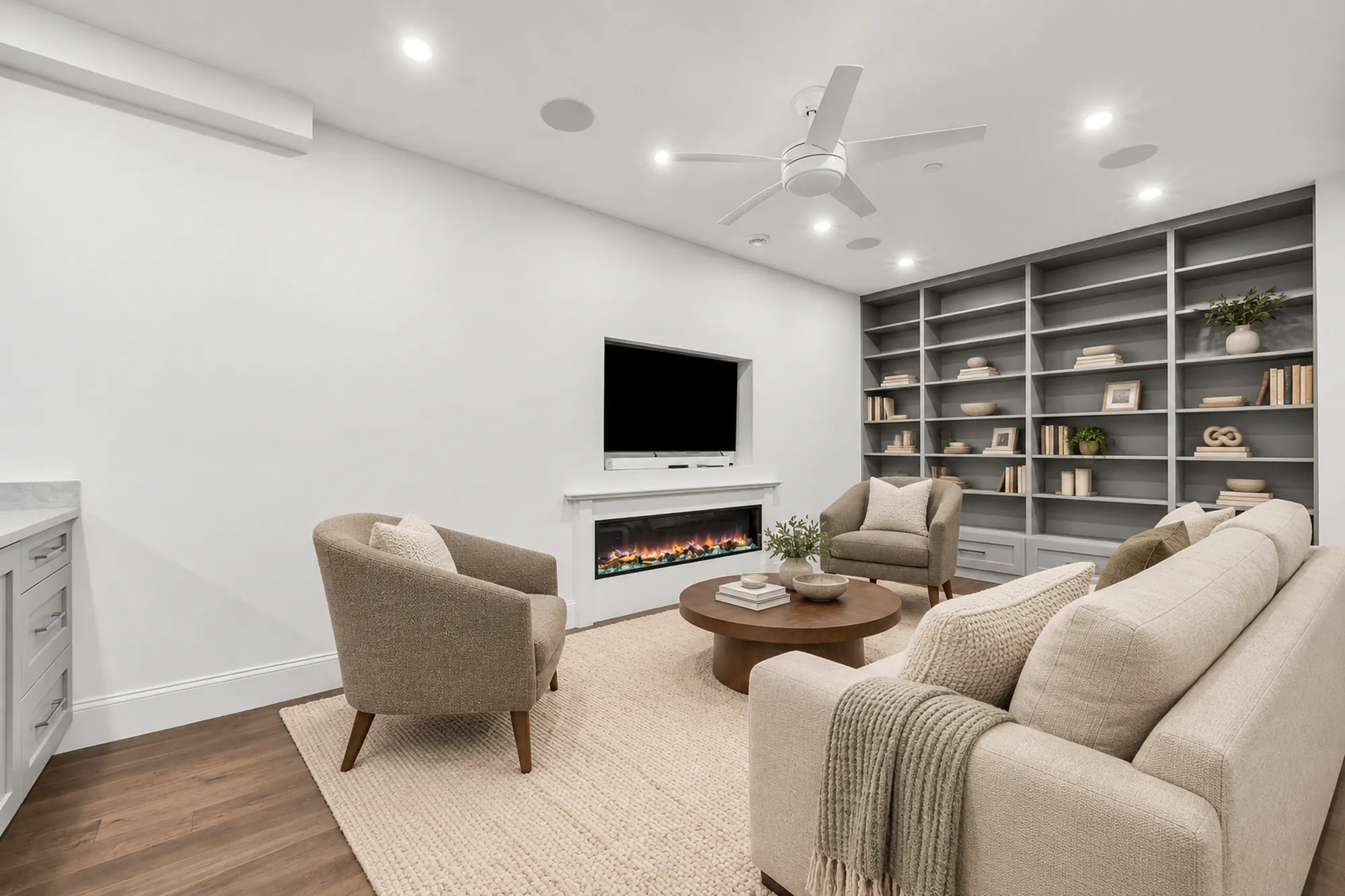 The family room virtually staged: a sofa and armchairs around a round coffee table, an electric fireplace under a television, built-in grey shelves