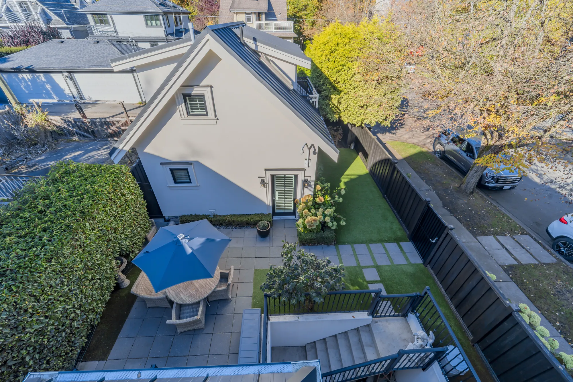 Looking down from the balcony: the patio with its umbrella and table, the turf and paths, the laneway house, the street at the side