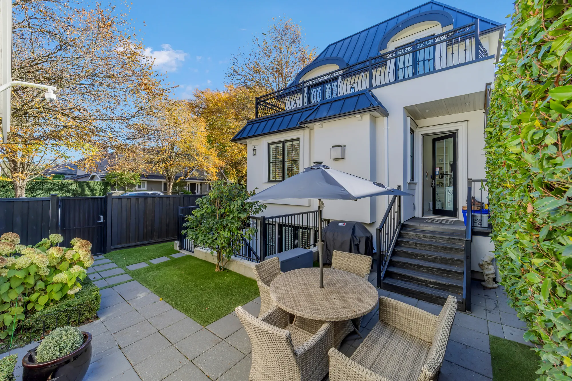 The back garden: a round table and wicker chairs under a blue umbrella, the steps up to the back door, hydrangeas in pots