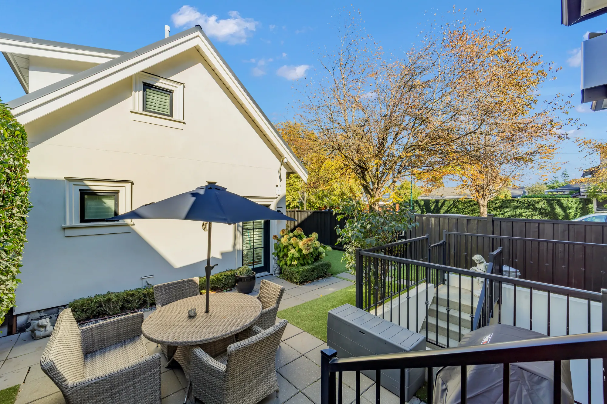 The garden at the side of the house: a table under an umbrella, a railing around the steps down to the lower floor