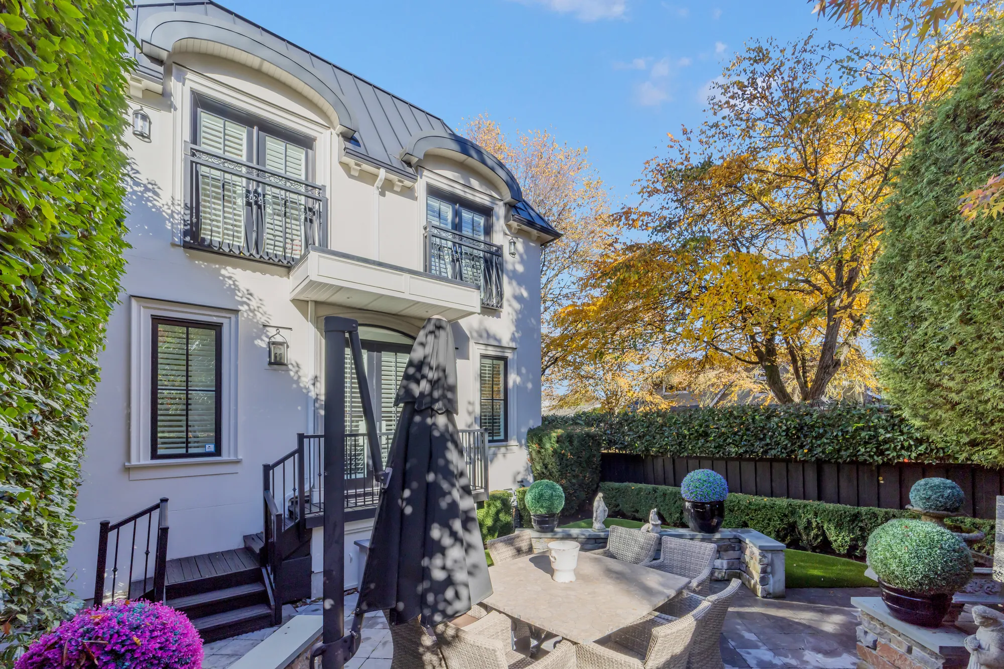 The side of the house with French doors and a Juliet balcony above the patio, the outdoor table and topiary below