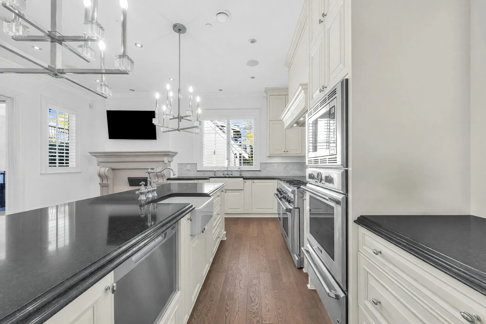 The kitchen along the island: a black counter, the sink, wall ovens, cream cabinets to the ceiling