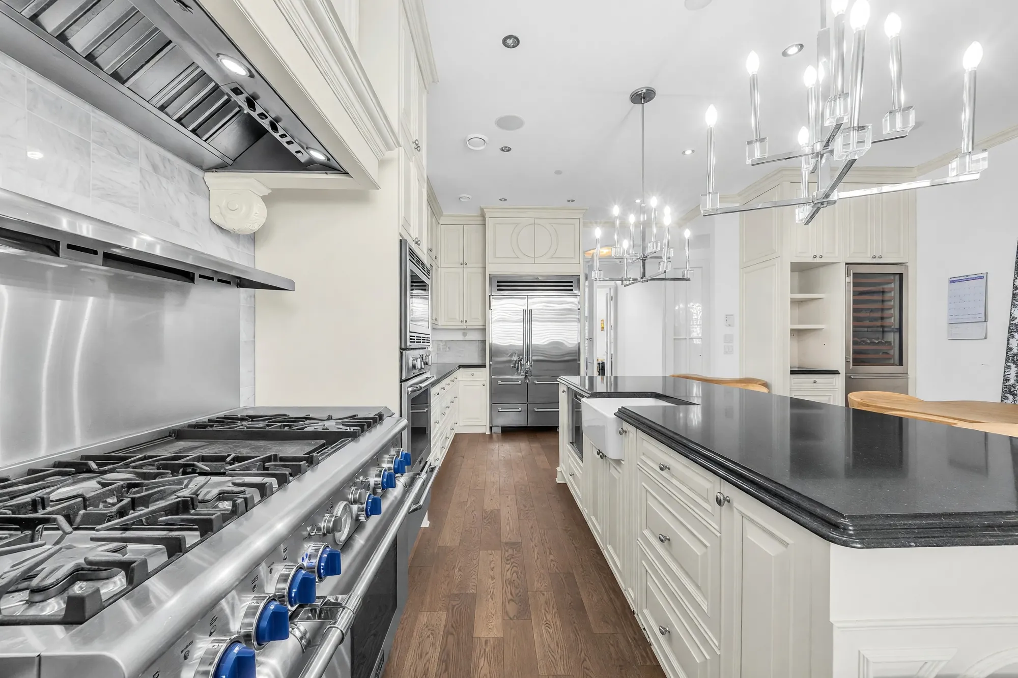 The range: a wide gas cooktop with blue knobs under a stainless hood and a steel backsplash, the island beside it