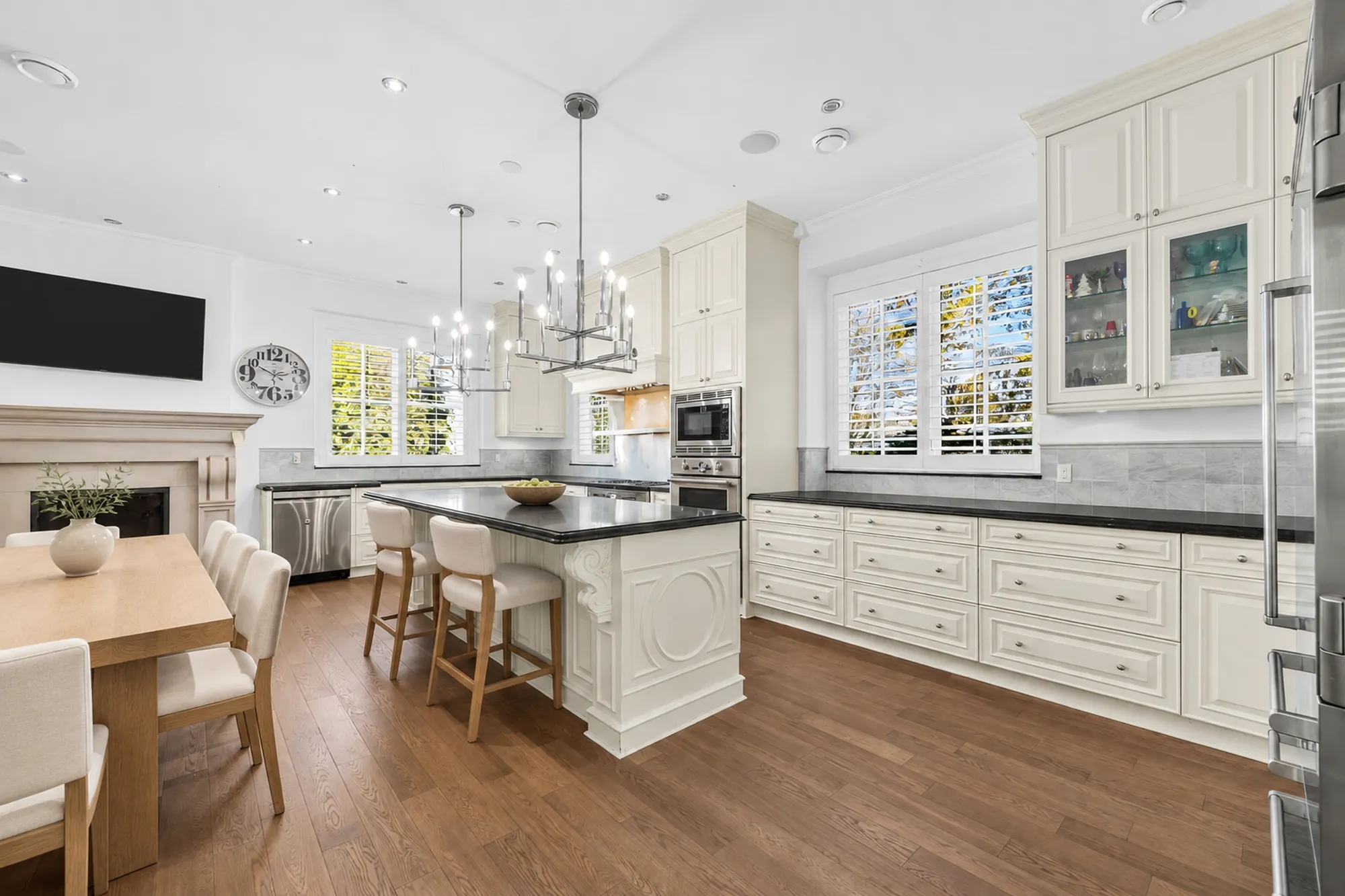 The kitchen and dining room virtually staged: a white island with a black counter, a wood dining table by a fireplace, pendant lights, cream cabinets and stainless appliances