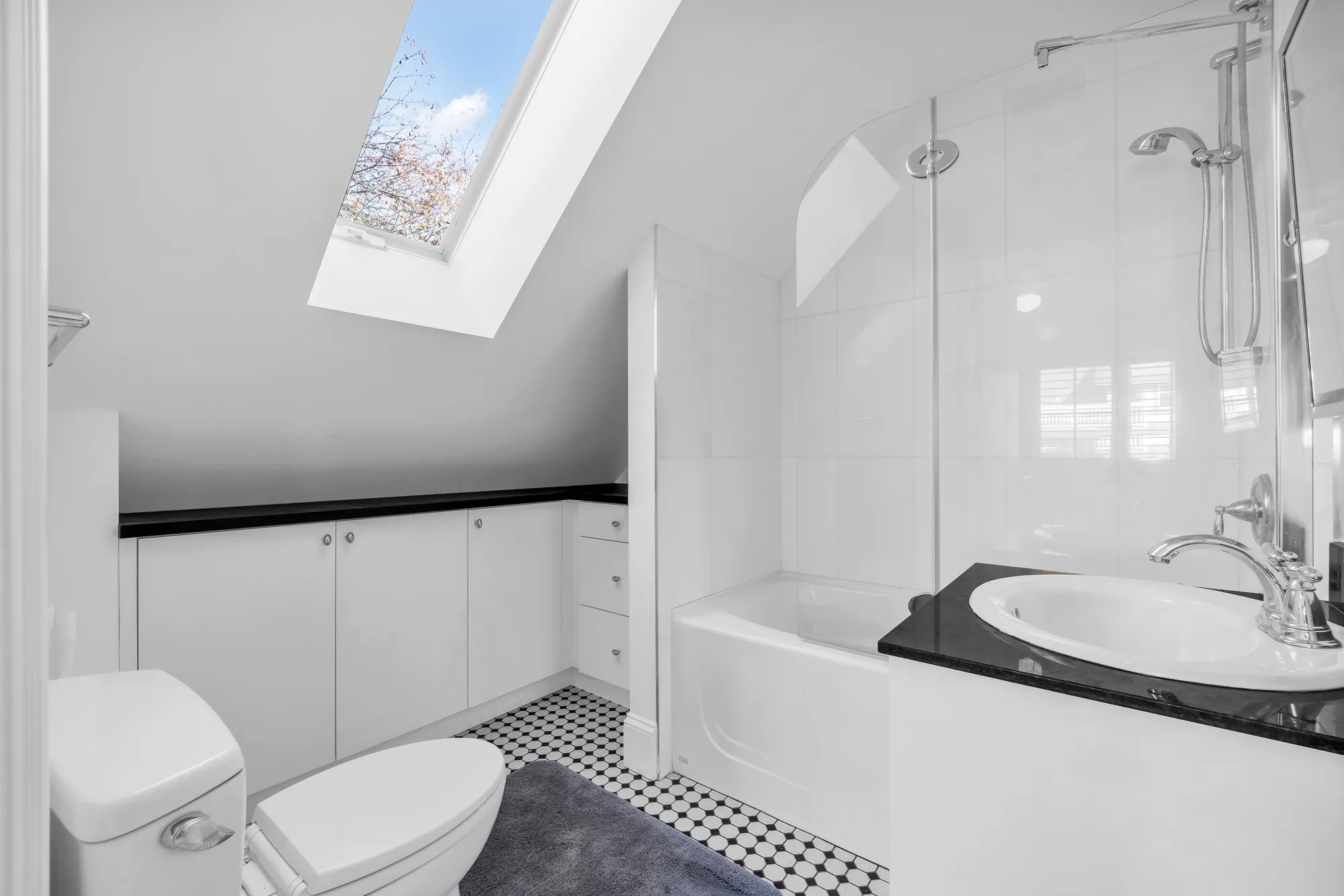 The laneway bathroom: a skylight in the sloped ceiling, a tub with a glass screen, a black counter and white cabinets