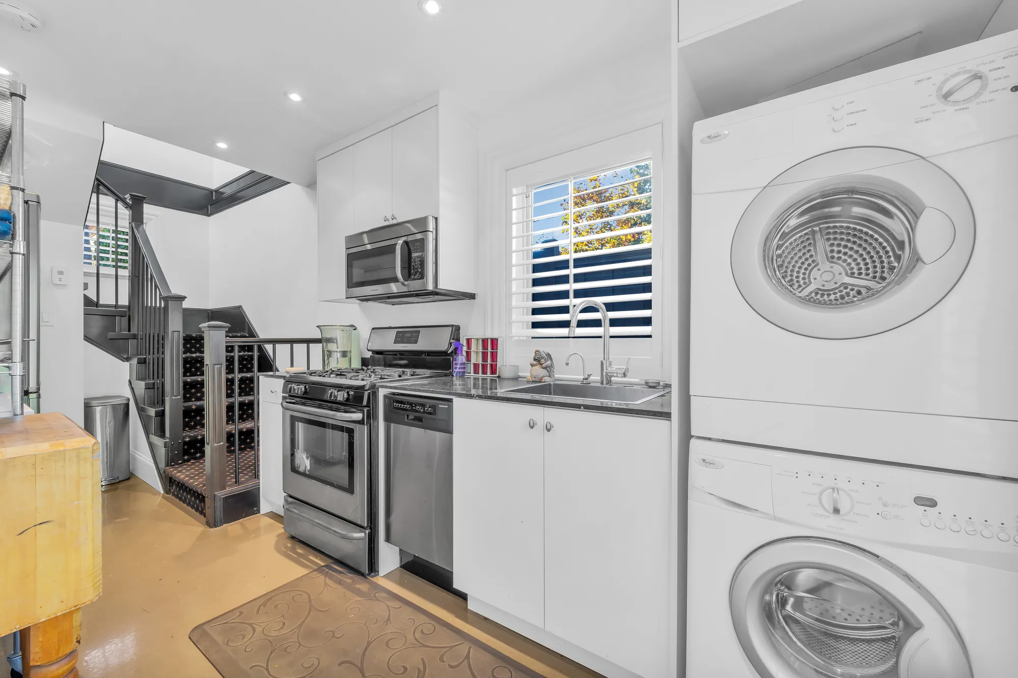 The laneway kitchen from the other end: the stairs up, the sink under a shuttered window, the stacked washer and dryer