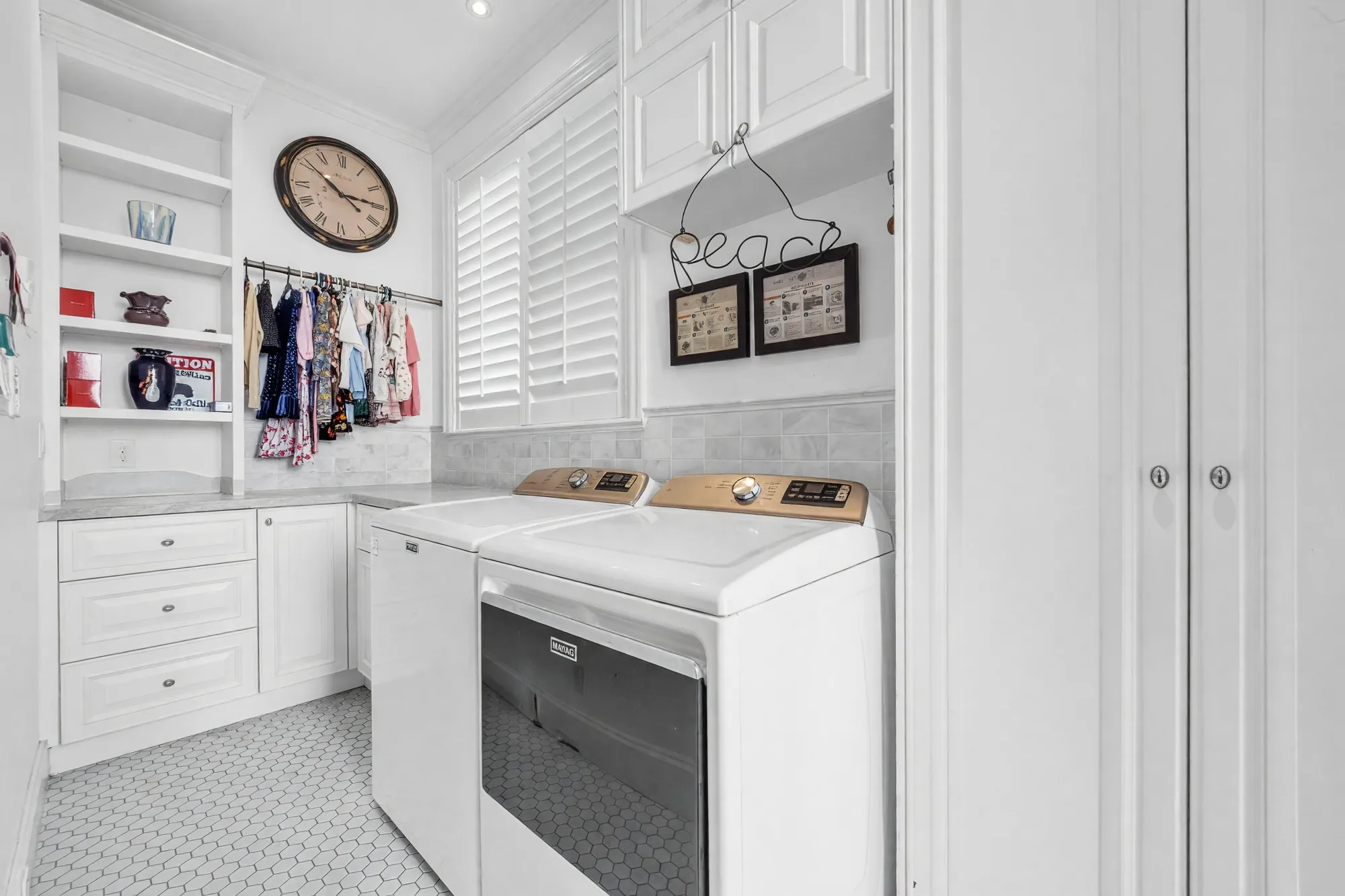 The laundry room: a washer and dryer, cream cabinets and open shelves, a hanging rail, a shuttered window and a clock