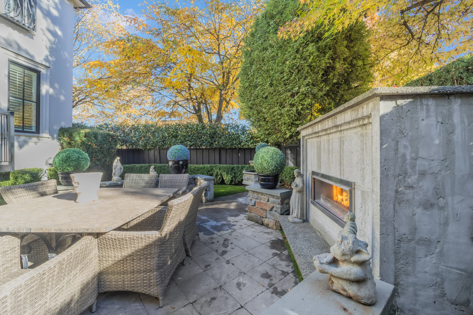 The outdoor fireplace in a stone surround beside the patio seating, a hedge behind