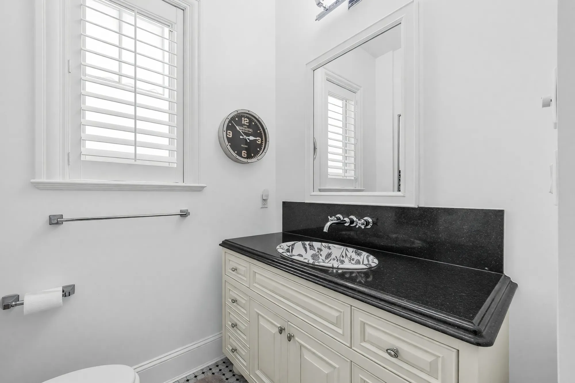 The powder room: a cream vanity with a black stone counter and a patterned vessel sink, a wall-mounted faucet, a shuttered window and a mirror