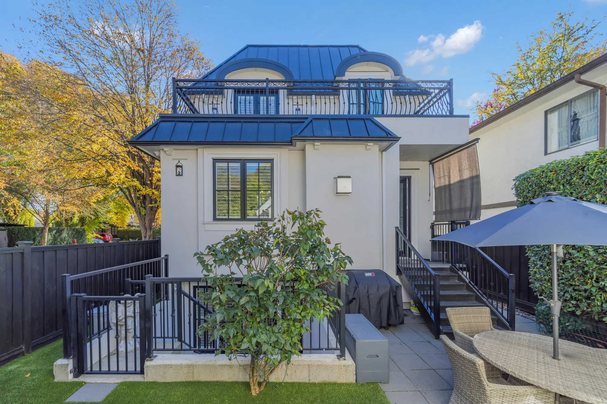 The back of the house: the rooftop railing at the top, a terrace, the steps down to the garden, an umbrella and outdoor furniture