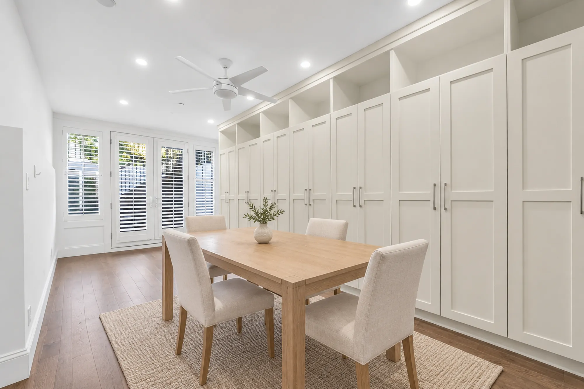 The recreation room virtually staged: a wood dining table with four upholstered chairs on a jute rug, a wall of built-in cabinets, French doors to the patio