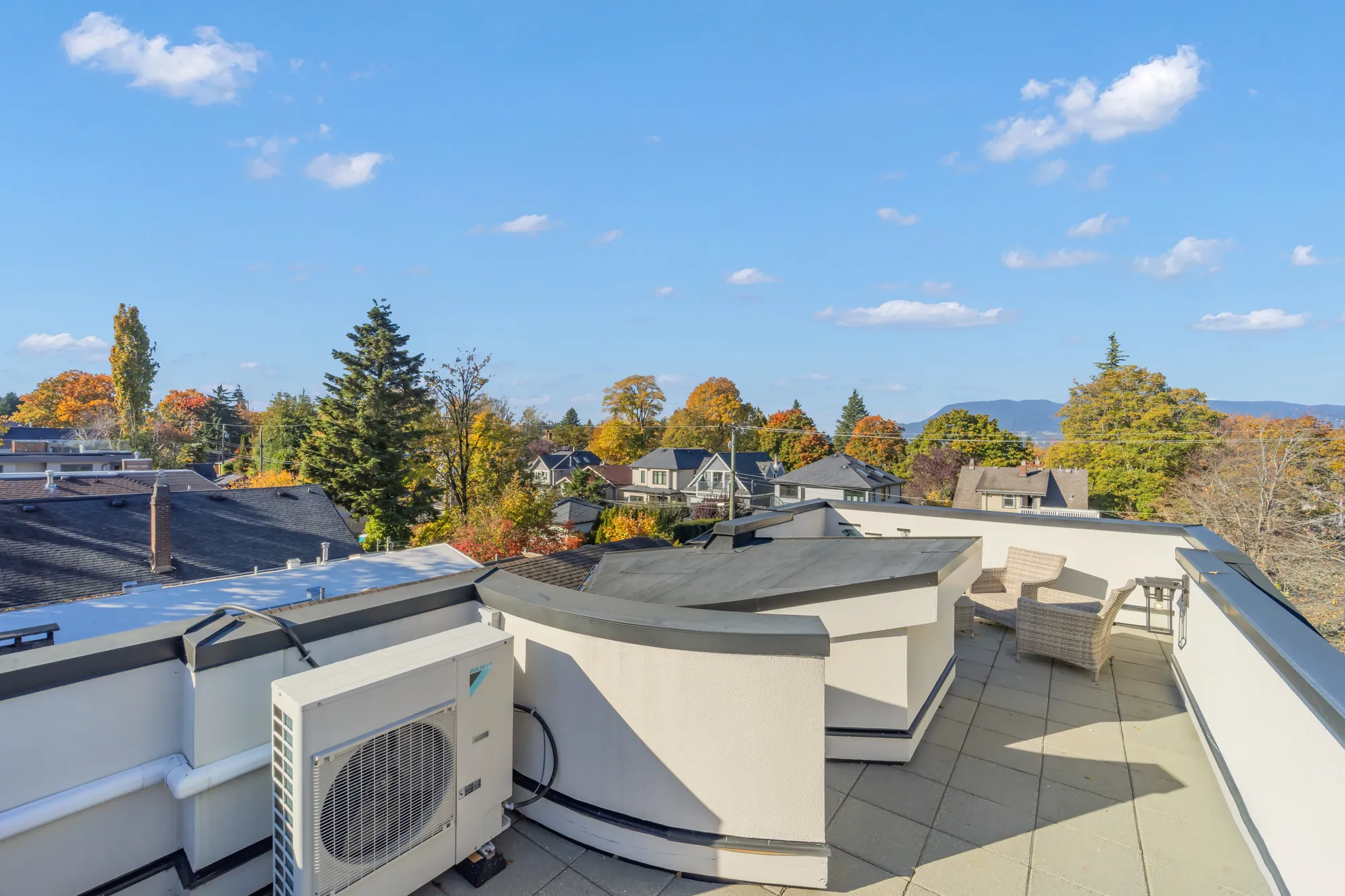 The roof deck toward the stair: a curved parapet, chairs, the heat pump unit, the mountains beyond the trees